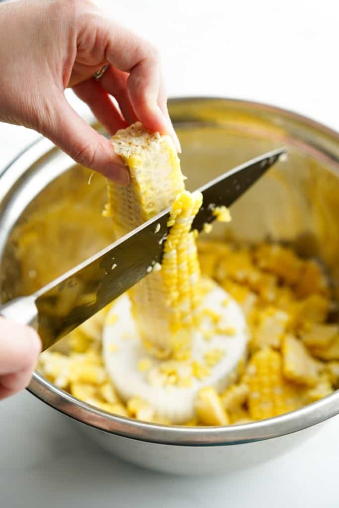 Slicing corn kernels off cob on an inverted small ramekin in a mixing bowl