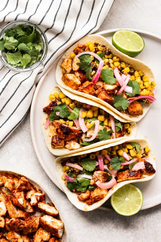 Top down view of three bbq chicken tacos topped with corn, cilantro and pickled red onions
