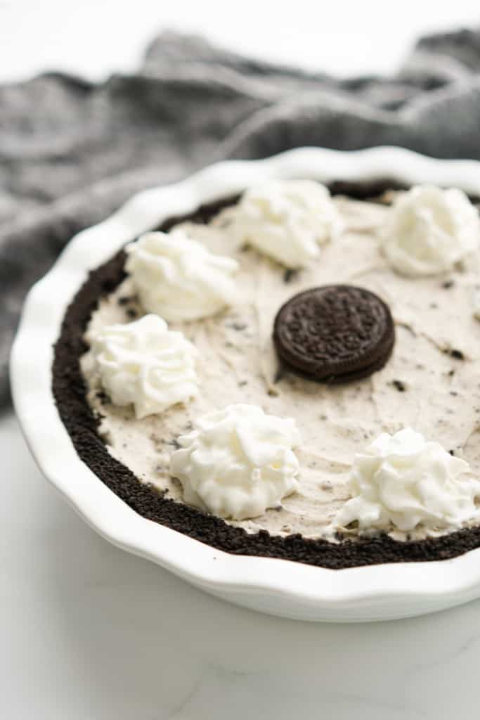 Cookies and cream pie in a pie pan topped with whipped cream and an Oreo cookie