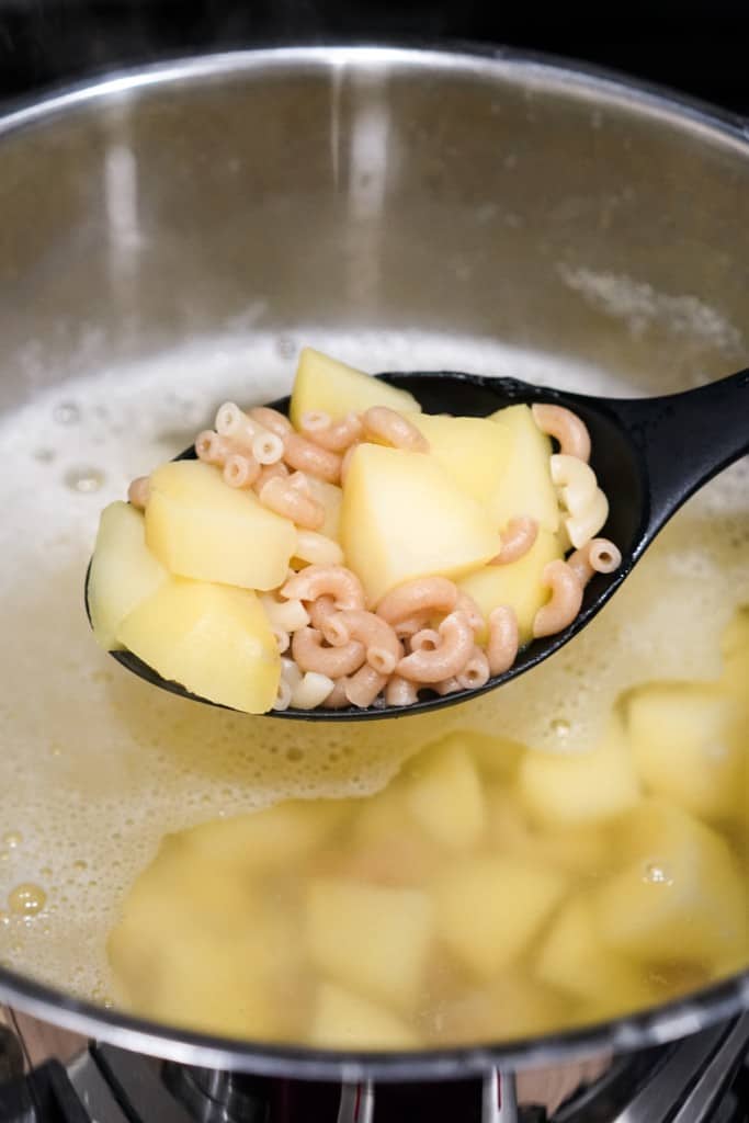 Boiling potato and macaroni together at the same time in water.