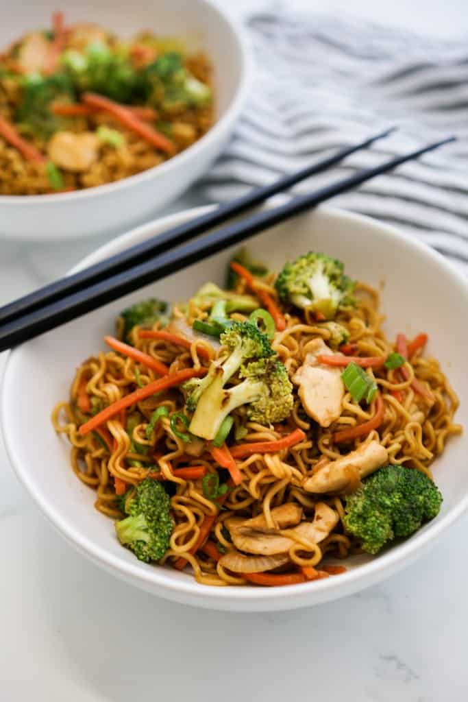 A plate of ramen noodles in a bowl topped with a pair of chopsticks sitting on the bowl