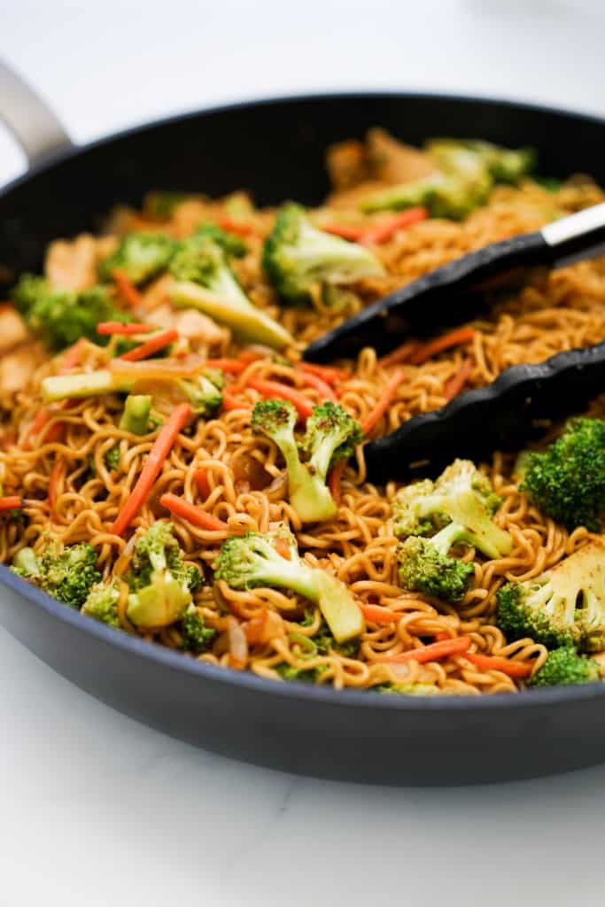 A skilet of ramen noodle stir fry with broccoli and carrots