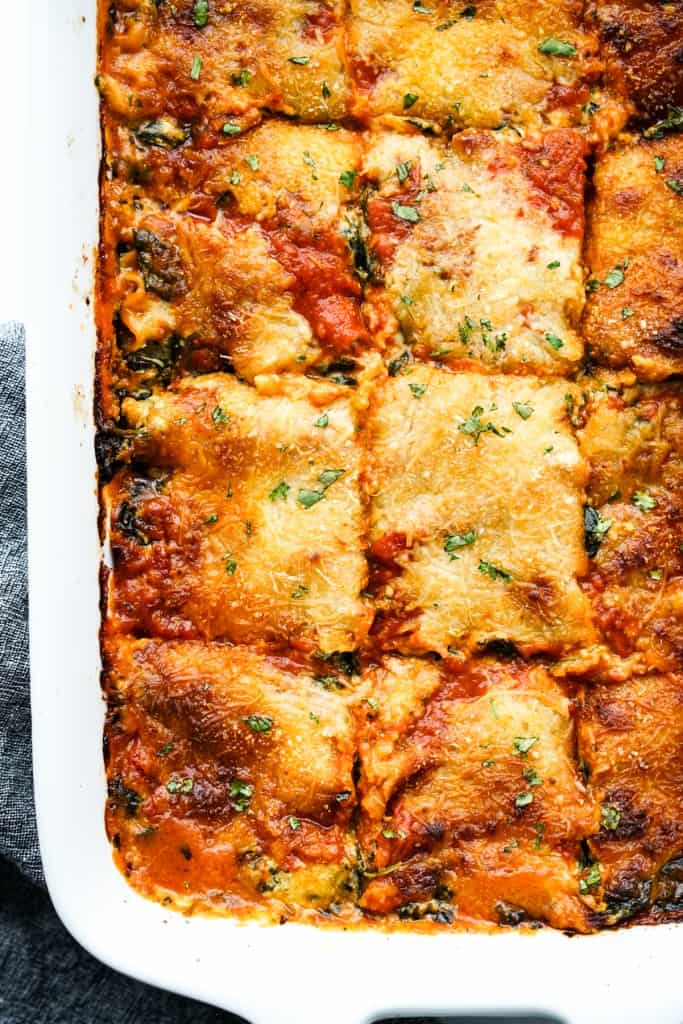 Top down image of a casserole dish of spinach lasagna sliced into square pieces