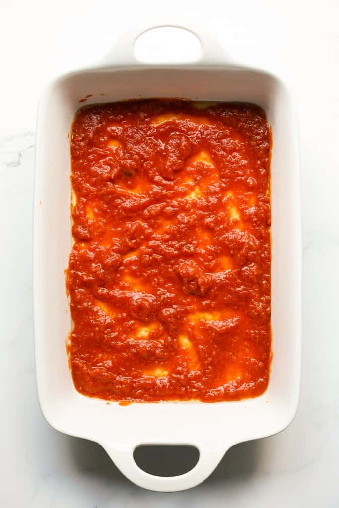 a layer of marinara sauce at the bottom of a casserole dish