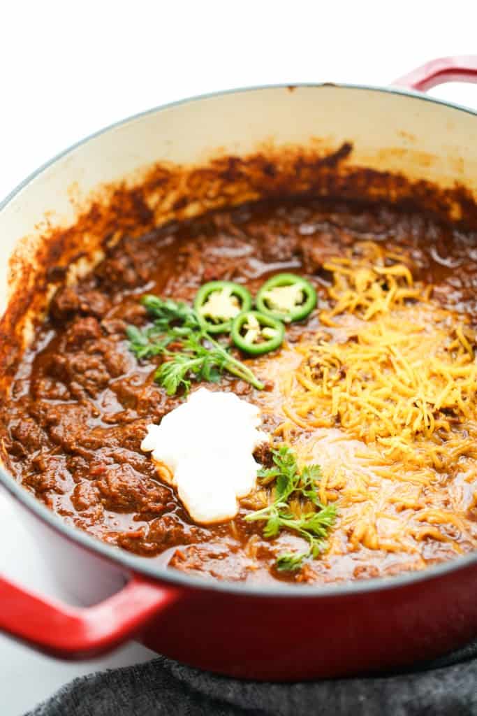 A bowl of chunky Texas style chili topped with cheese, sour cream, jalapeño and cilantro 