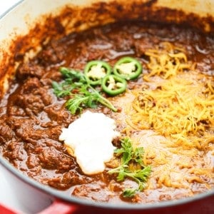 A large pot of chili topped with cheese, sour cream and jalepeno