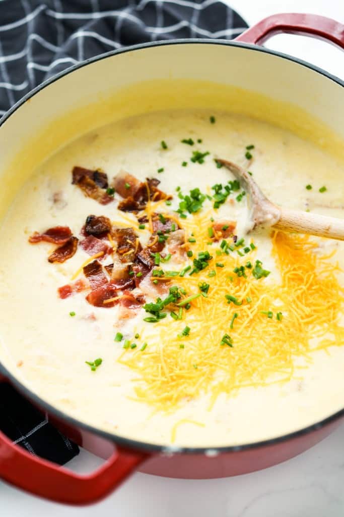 A large pot of thick potato soup topped with shredded cheese, bacon pieces and chives