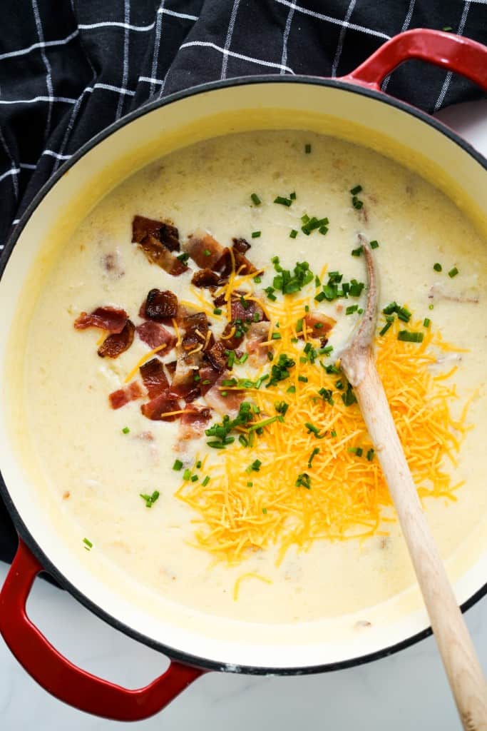 A Dutch oven filled with creamy potato bacon soup topped with bacon, cheese and chives