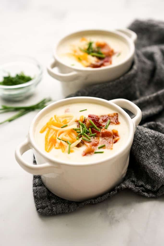 Two bowls of potato bacon soup topped with bacon, cheddar cheese and chives