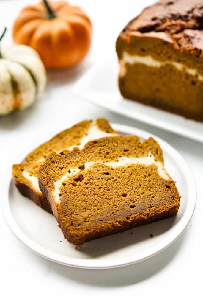 Two slices of pumpkin cream cheese swirl bread on a plate, with a loaf in the background