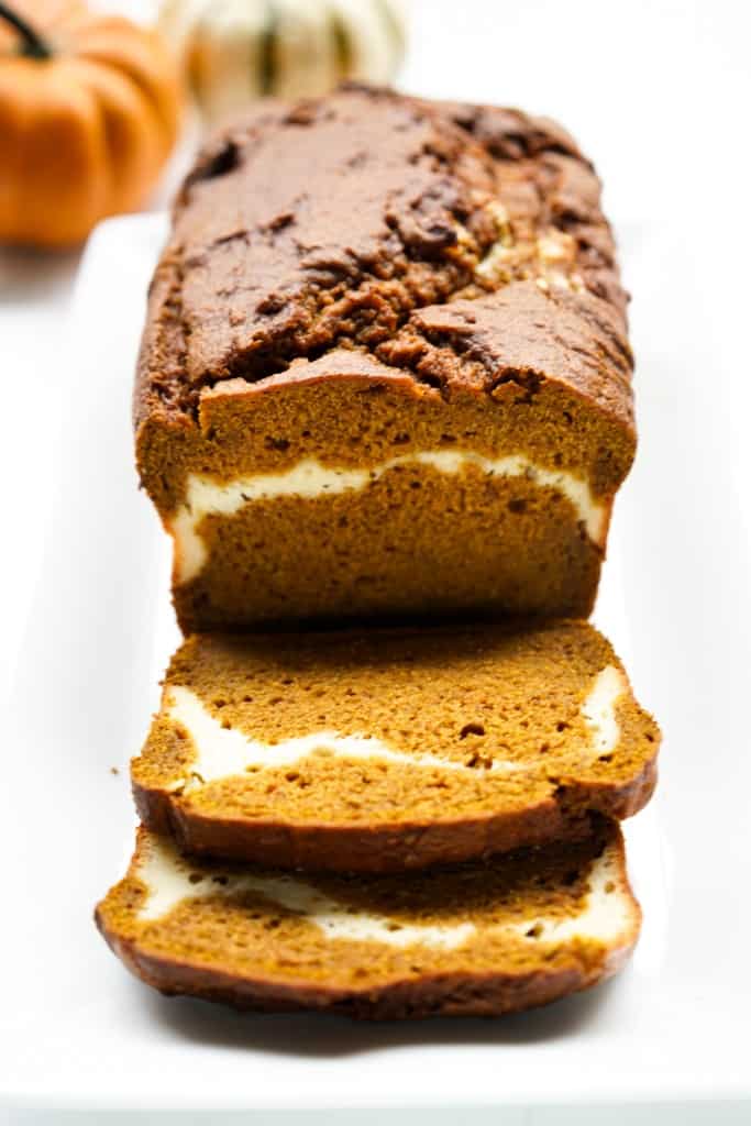 A loaf of pumpkin bread with cream cheese swirls sliced into a few pieces