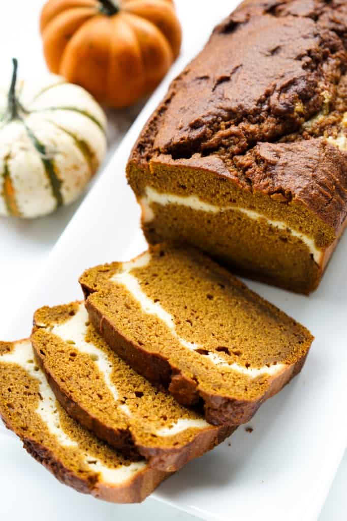 A loaf and a few slices of pumpkin bread with swirls of cream cheese inside