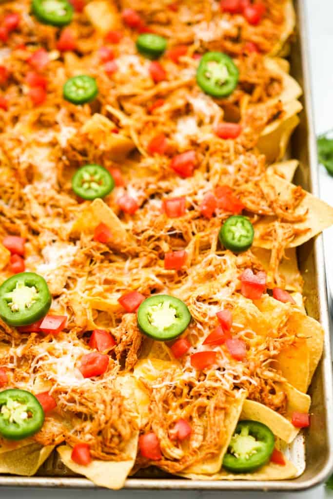 Sheet pan nachos topped with chicken, cheese, jalapeno, and tomatoes