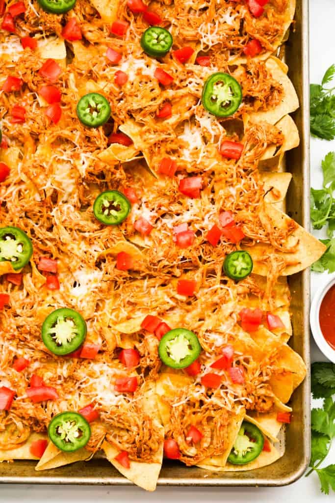 Top down view of a sheet pan shredded chicken nacho topped with cheese, tomatoes and jalapeno
