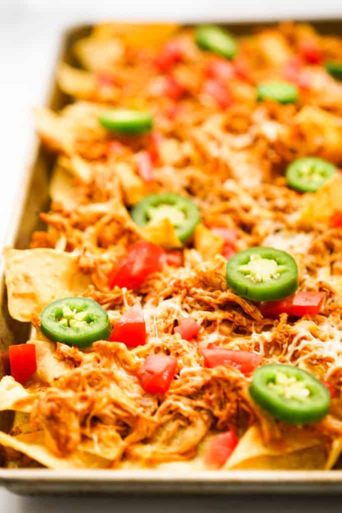 Sheet pan shredded chicken nachos topped with cheese, jalapeno and tomatoes.