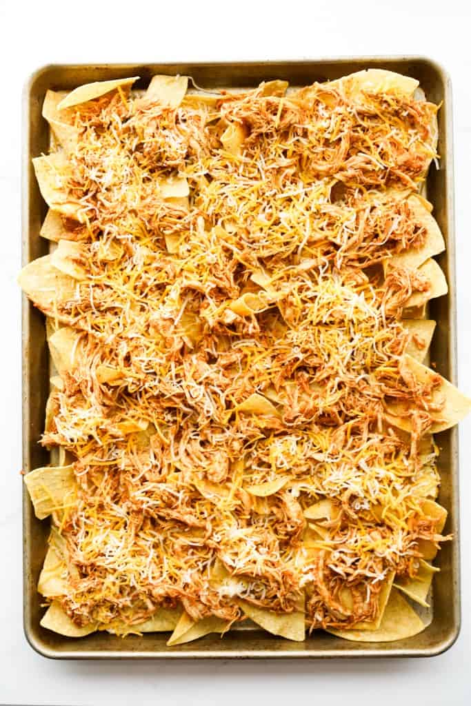 tortilla chips topped with pulled chicken and cheese on a large sheet pan