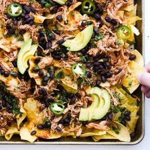 Sheet pan topped with tortilla chips, melted cheese, tomatoes and jalapenos