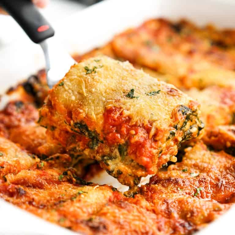 Lifting out a piece of lasagna layered with spinach, red sauce and cheese.