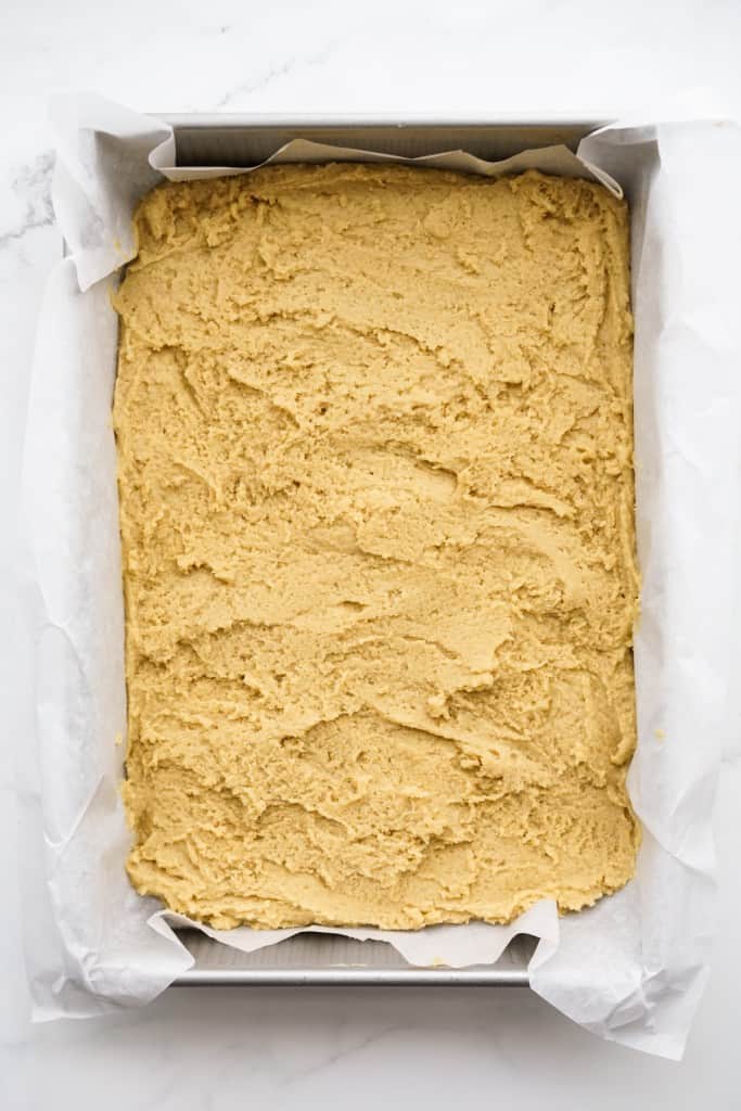 Dough being spread out on a rectangular baking dish lined with parchment paper