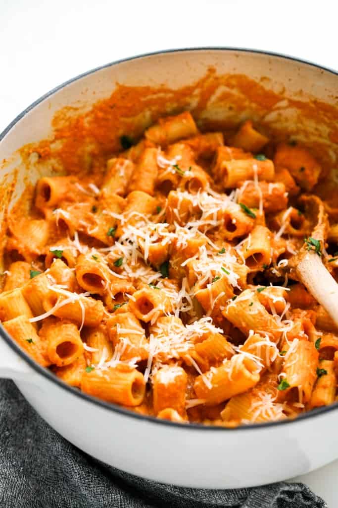 A wooden spoon in a large pot of rigatoni pasta tossed in creamy pumpkin sauce.
