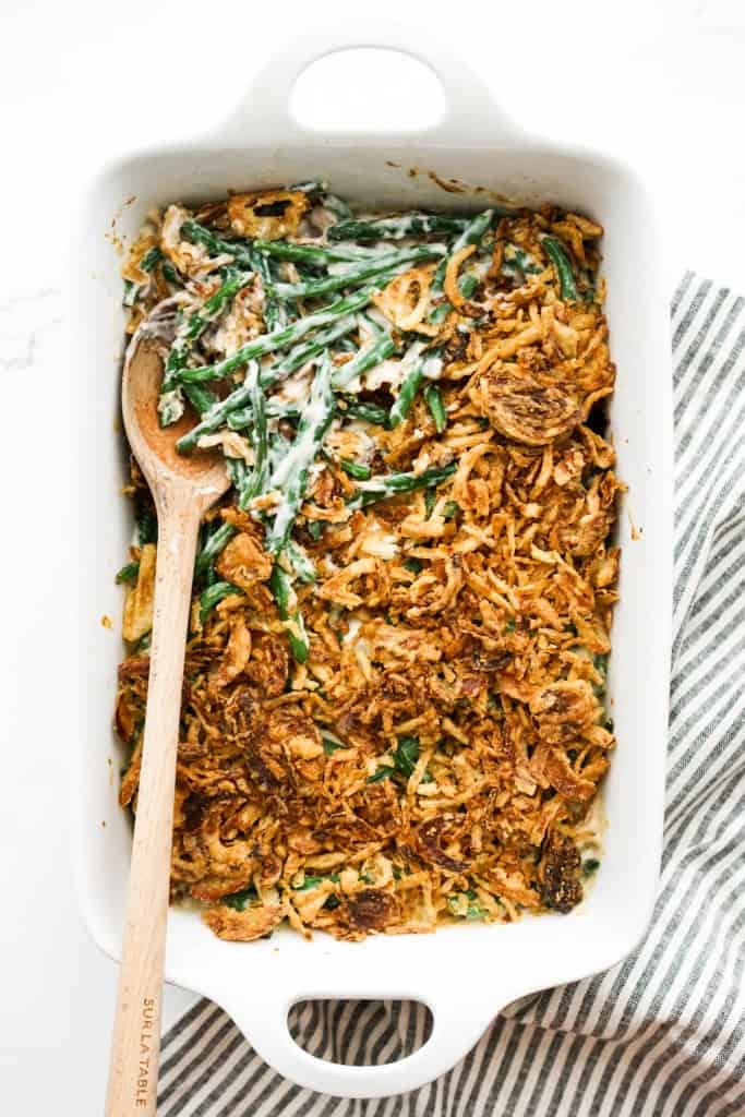 A large rectangular casserole dish of green bean casserole with fresh green beans, topped with fried onions