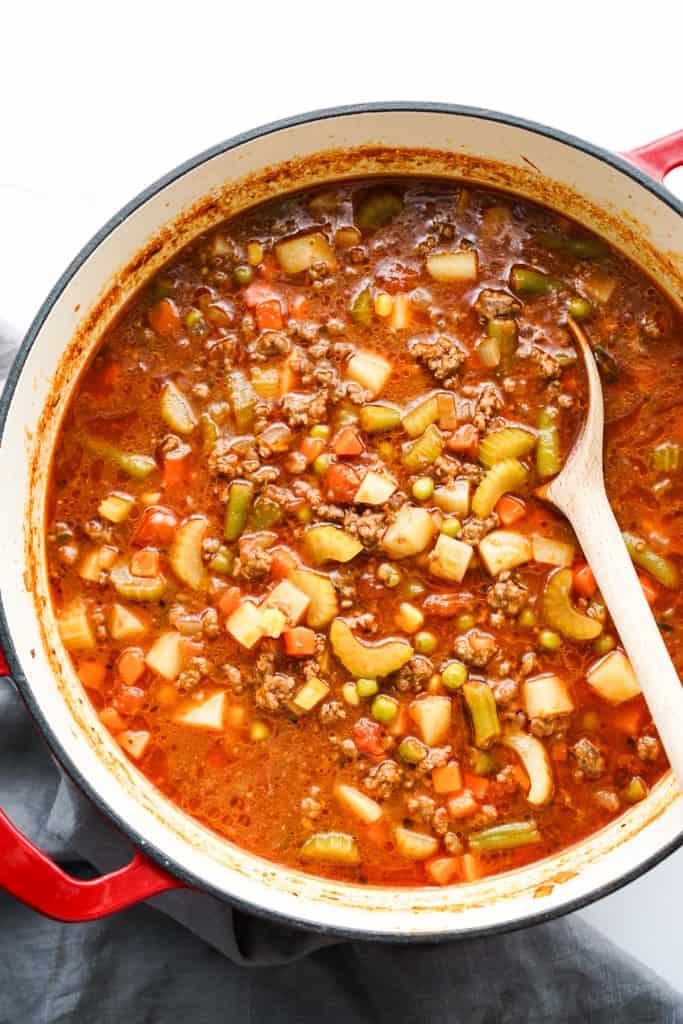 A large pot of ground beef vegetable soup loaded potatoes, green peas, carrots and tomatoes