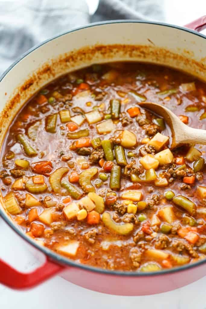 A large pot of vegetable ground beef soup in a red Dutch oven