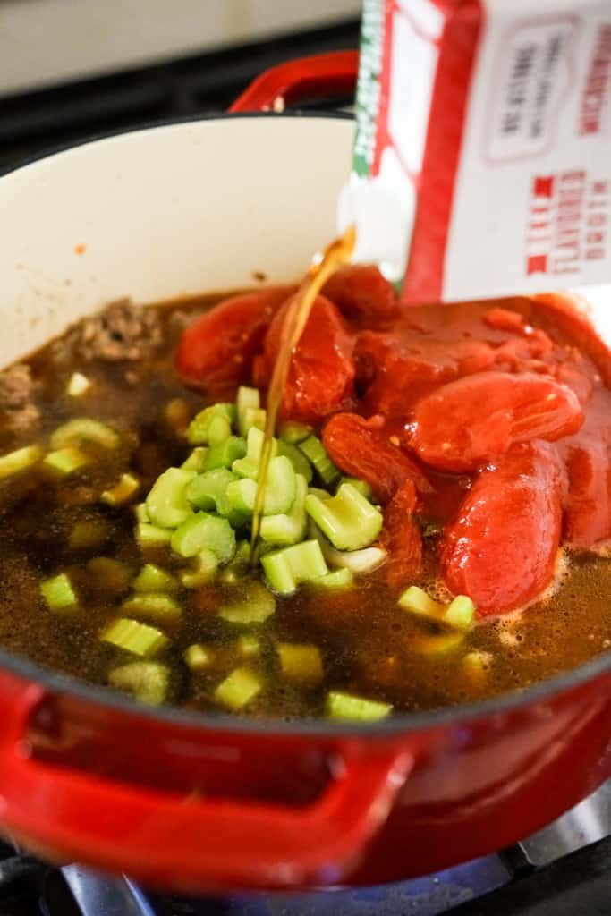 Adding beef broth to Dutch oven filled with tomatoes and celery