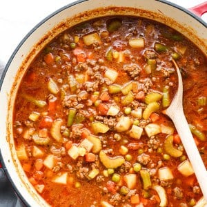 A pot of chunky soup filled with ground beef, celery, potatoes and tomatoes.