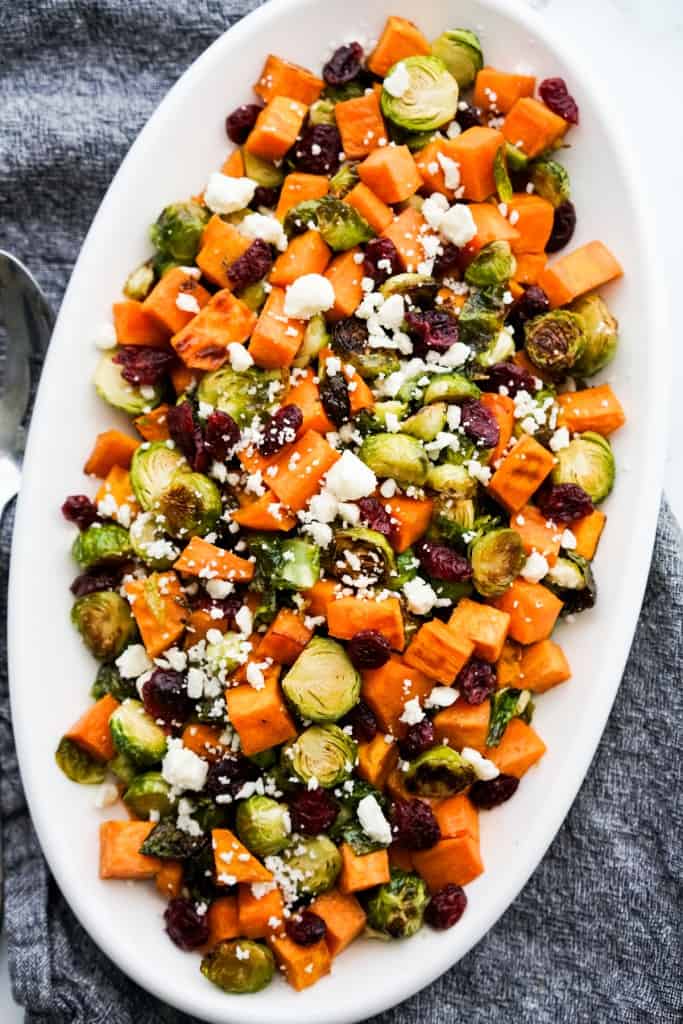 Closeup of a long oval plate of oven baked brussels sprouts, sweet potatoes, dried cranberries and feta cheese
