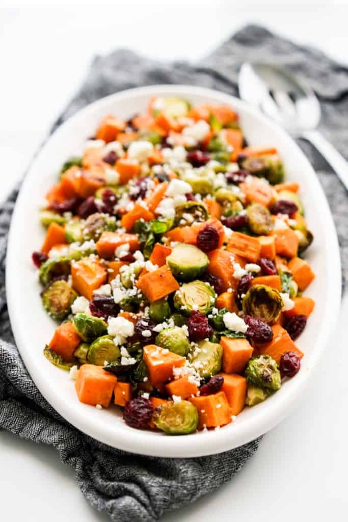 A platter of roasted brussels sprouts and sweet potatoes topped with dried cranberries and feta
