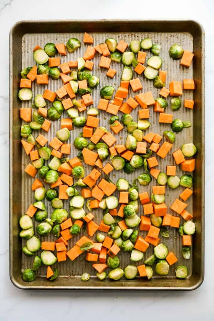 Cubed sweet potatoes and halved Brussels sprouts on a baking sheet