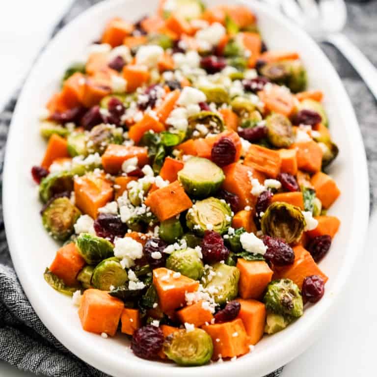 An oval plate of roasted brussels sprouts and sweet potatoes topped with dried cranberries and feta crumbles