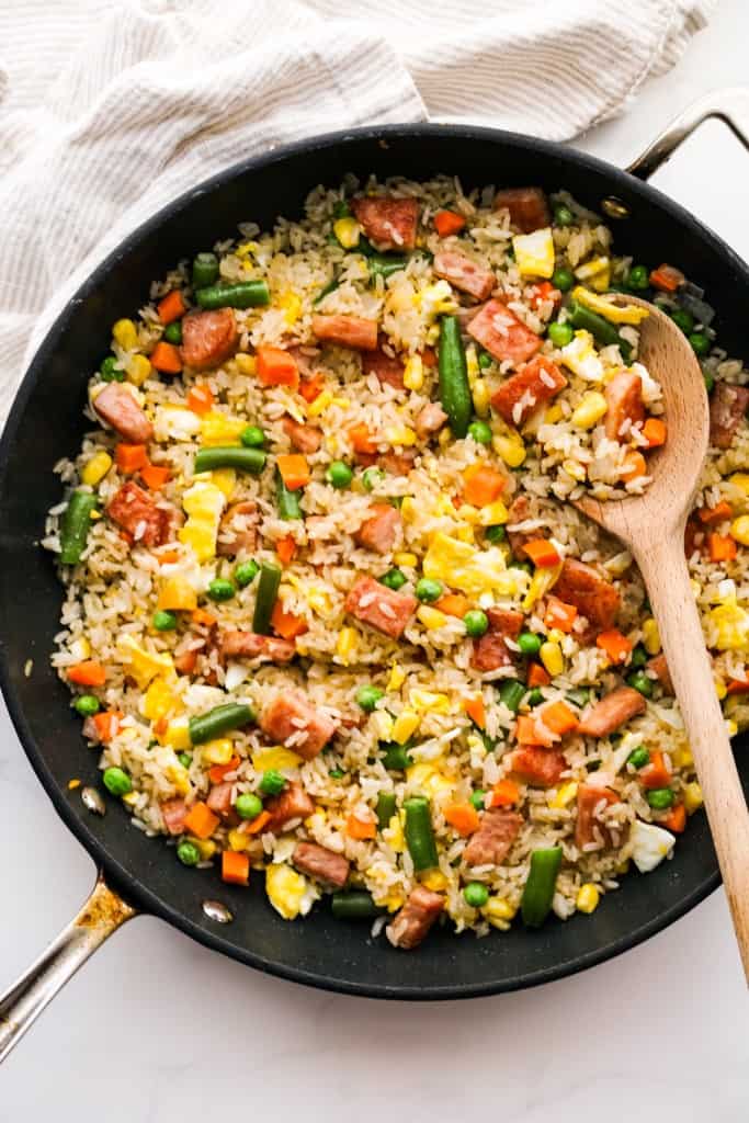 A skillet of fried rice with spam veggies and eggs