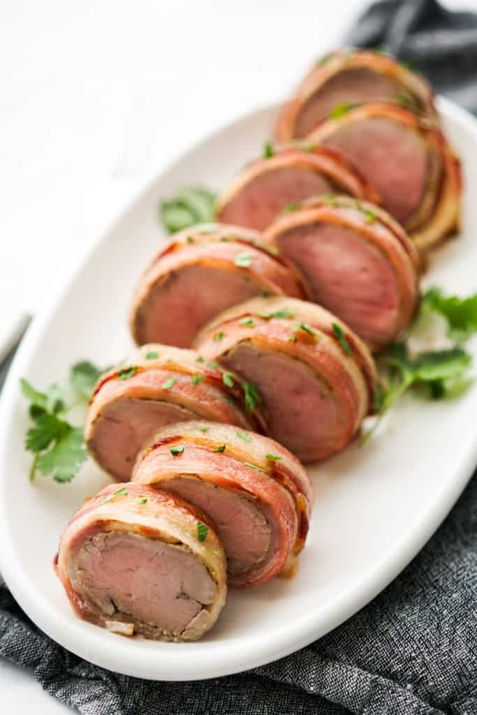 Sliced pieces of bacon wrapped pork tenderloin on an oval platter