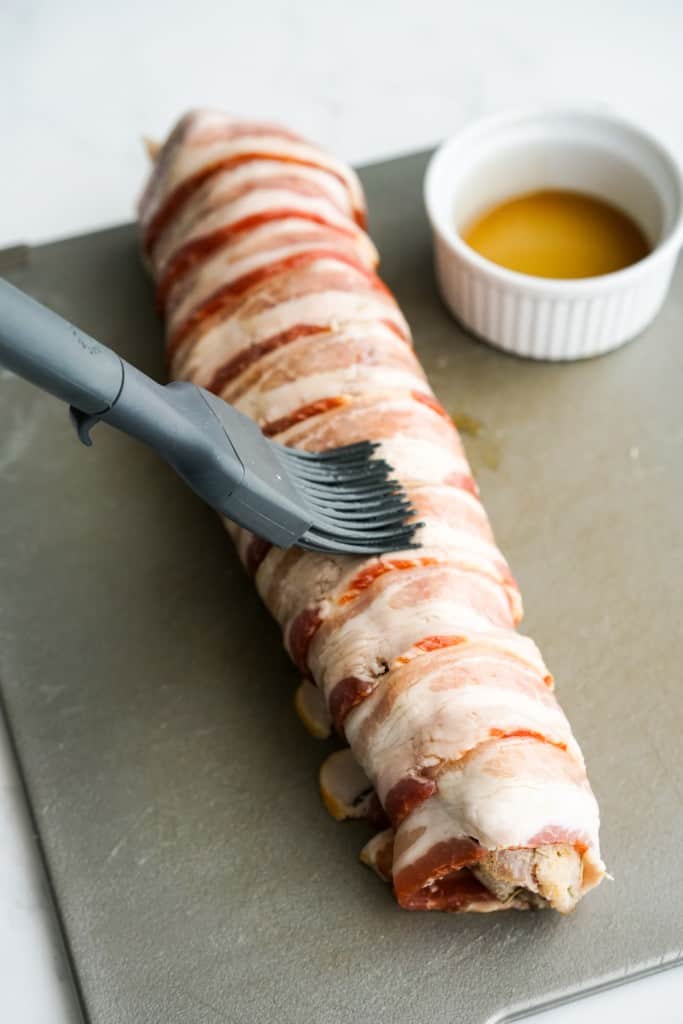 Brushing pork loin wrapped in bacon with maple syrup