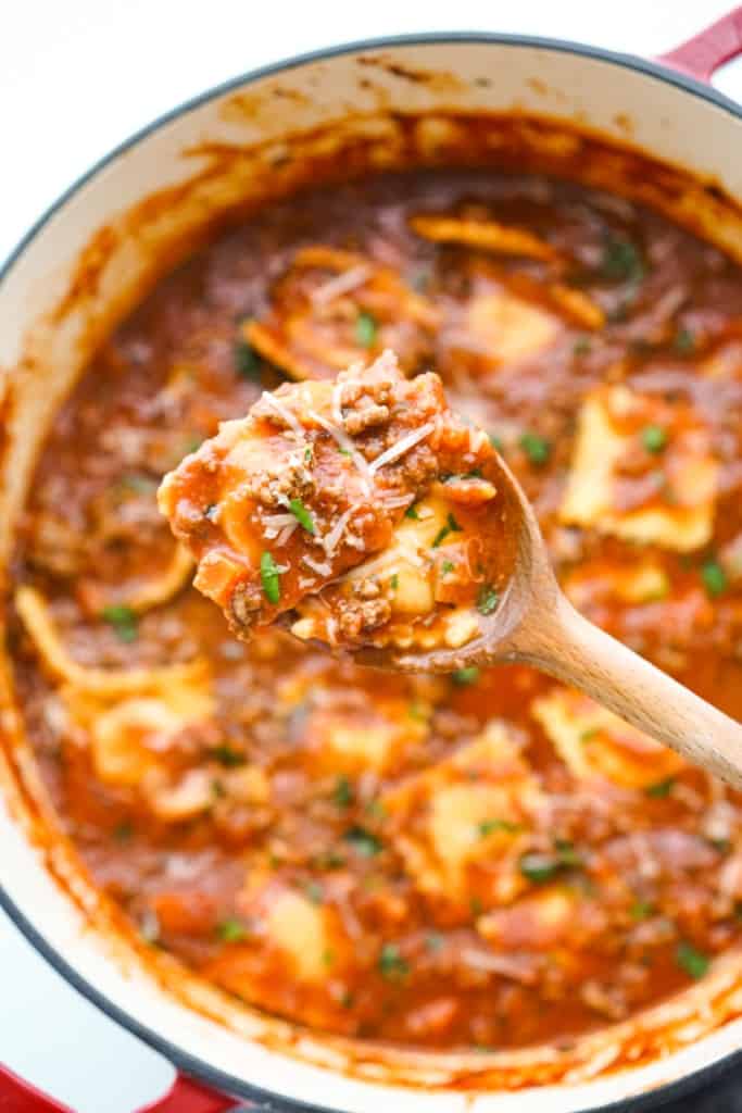 Scooping up some raviolis from a pot of soup using a wooden spoon