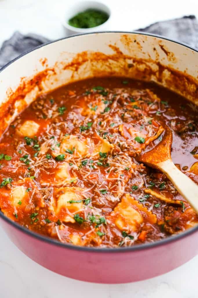 A pot of thick and chunky tomato ravioli soup with ground beef, and a wooden spoon sticking in it