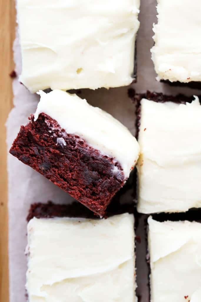 Closeup of red velvet brownies loaded with chocolate pieces and topped with cream cheese icing.