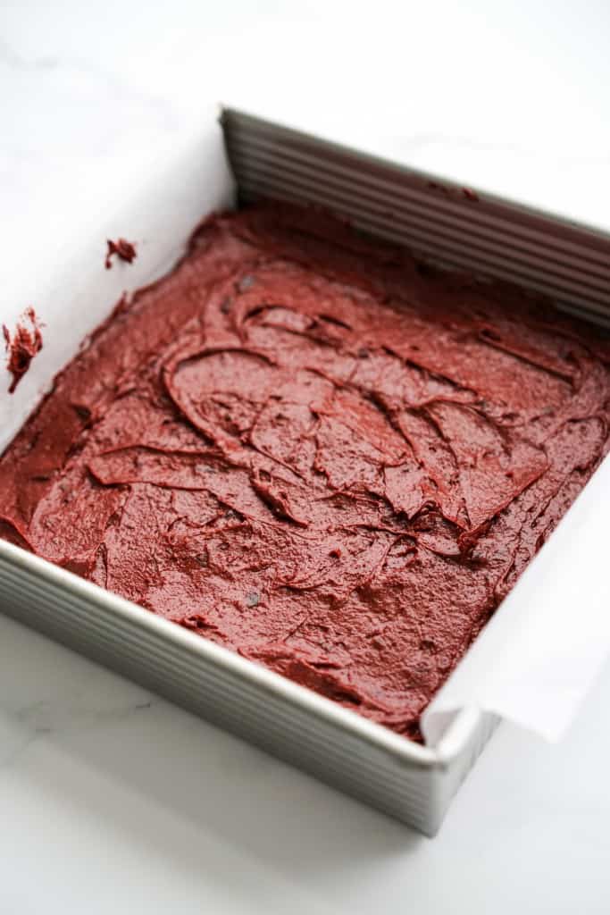 Red brownie mix in a square baking dish lined with parchment paper