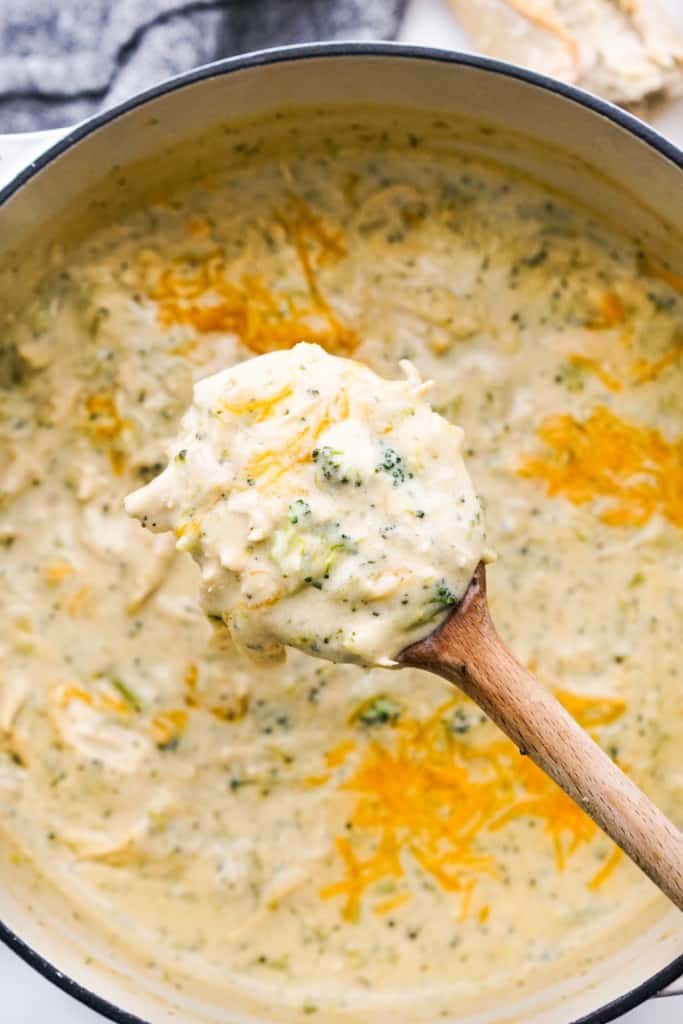 lifting up a spoonful of chicken broccoli cheddar soup from a large pot