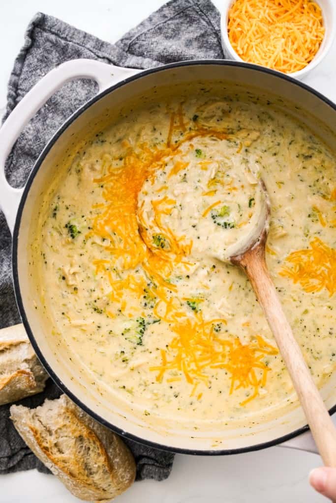 A large pot of chicken broccoli cheddar soup from a top down view with a w wooden spoon.