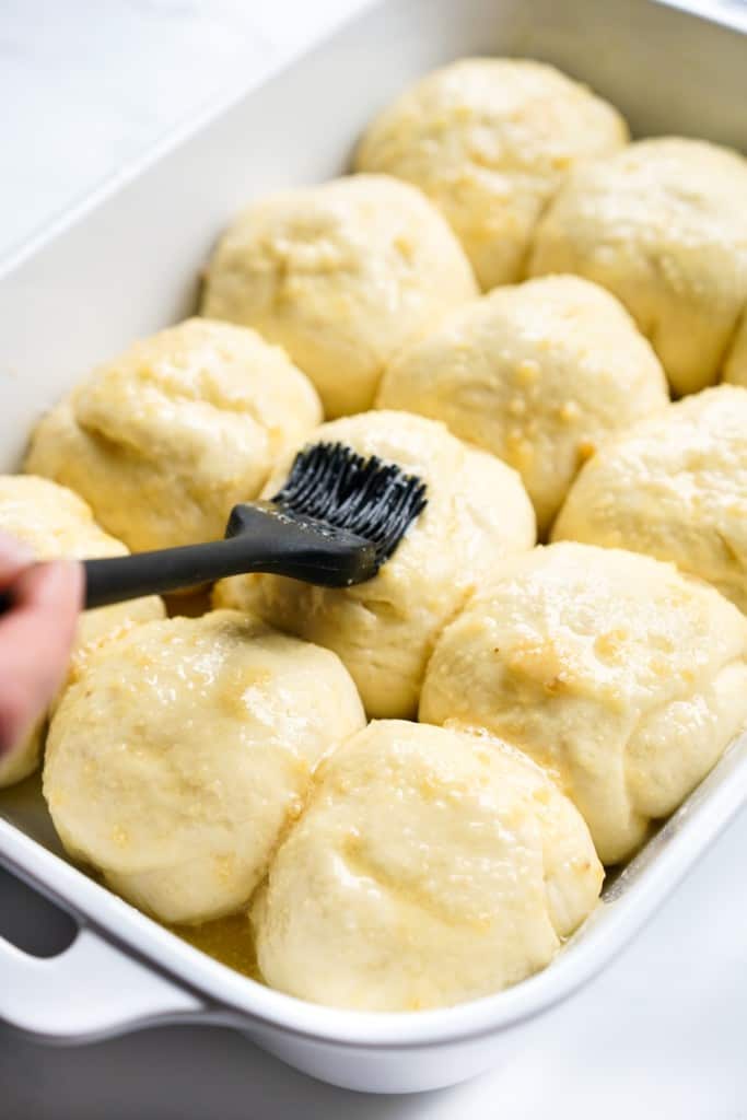 Brushing the tops of unbaked yeast rolls with garlic butter mixture