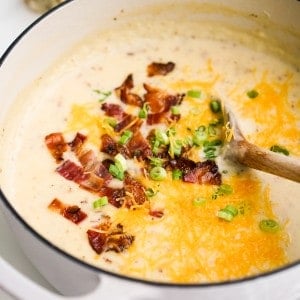 A pot of mashed potato soup topped with bacon, cheddar and green onions