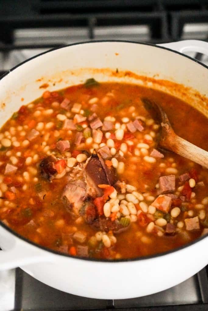 A large pot of navy bean soup with ham hock in the pot on the stove