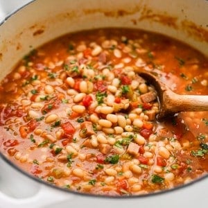 Stirring a pot of navy bean and ham soup with a wooden spoon