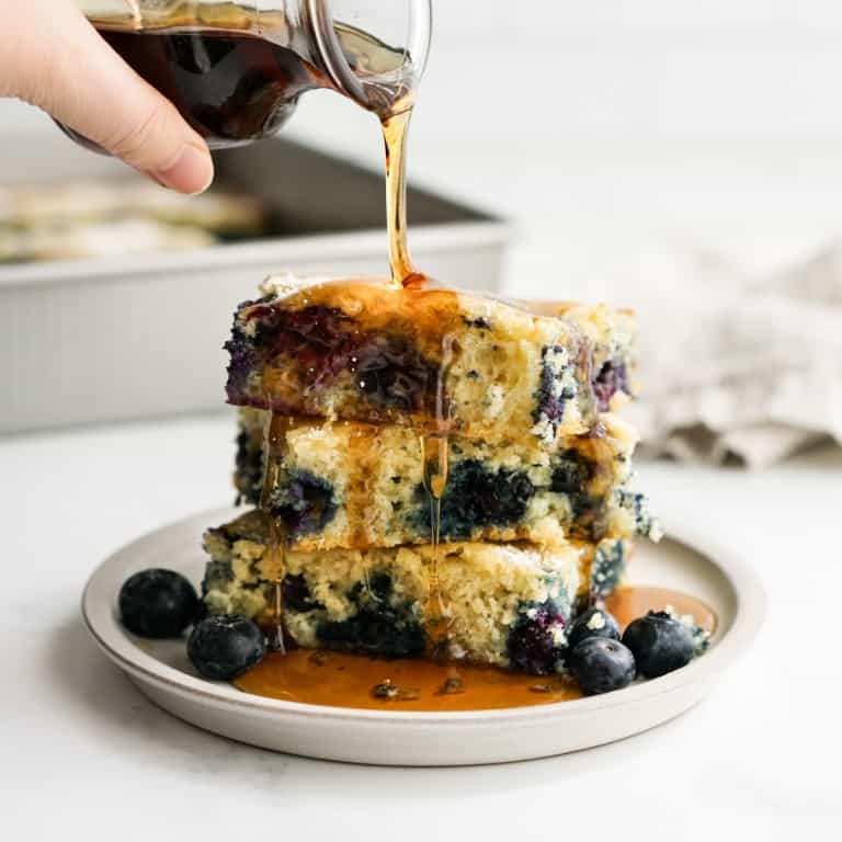 Pouring maple syrup on a stack of square blueberry pancakes