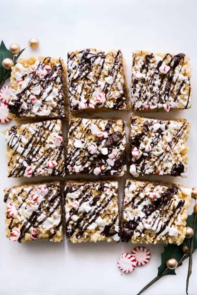 nine square pieces of rice krispie treats topped with chocolate drizzle, white chocolate drizzle, and crushed candy cane