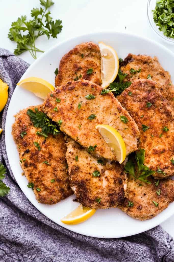 A plate of garlic parmesan crusted pork chops with lemon wedges