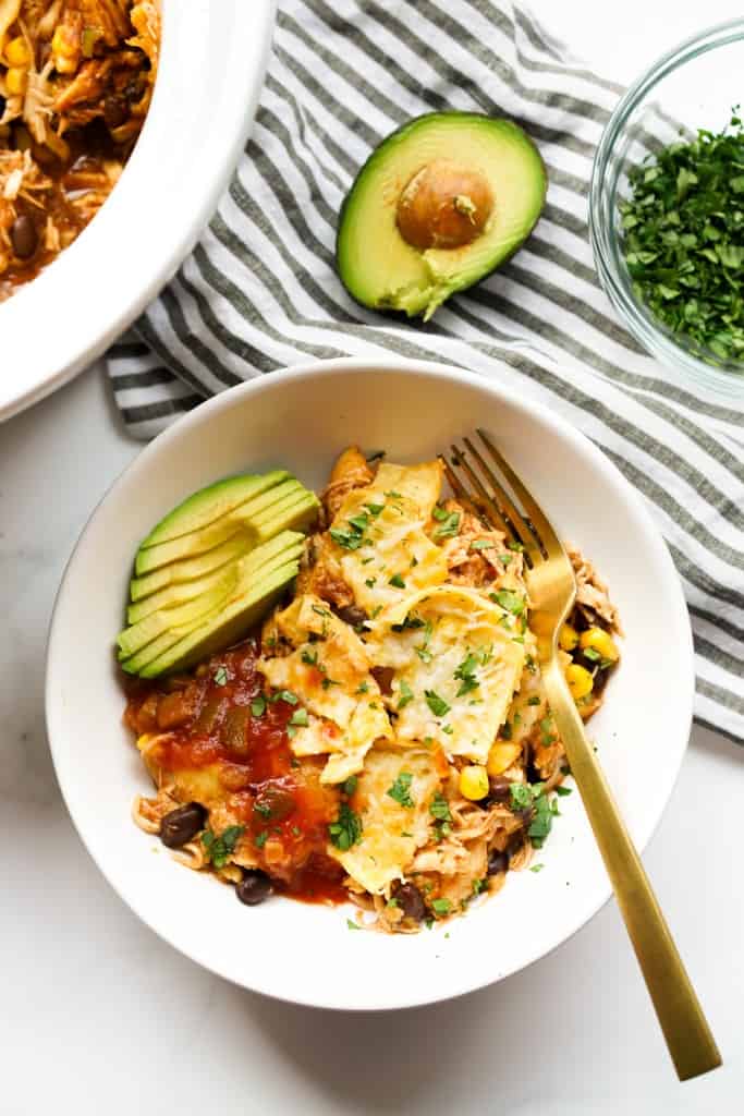 A bowl of chicken enchilada casserole topped with sliced avocado and salsa